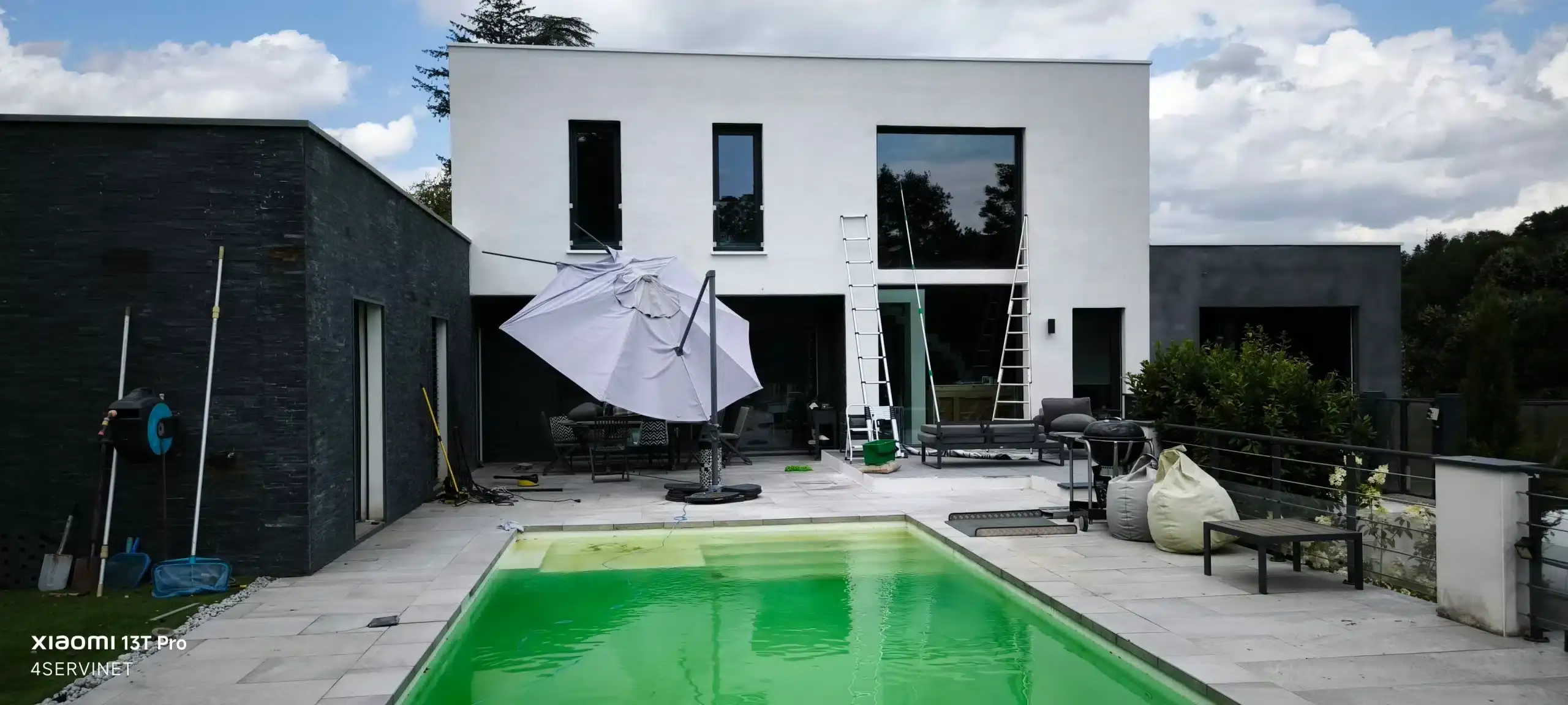 Image représentant un professionnel du nettoyage de vitres à domicile utilisant un seau, des raclètes, une échelle et une perche pour nettoyer efficacement des vitres.