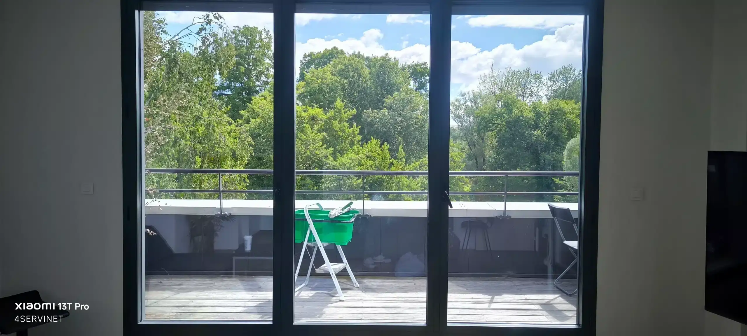 Une personne utilisant un seau, une raclette et une marche-pied pour nettoyer des vitres parfaitement propres, sans aucune trace visible.