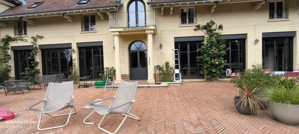 Image actuelle : Ouvrier utilisant un seau avec raclette, une échelle et un scarbot pour nettoyer les vitres d'une maison à Lyon.